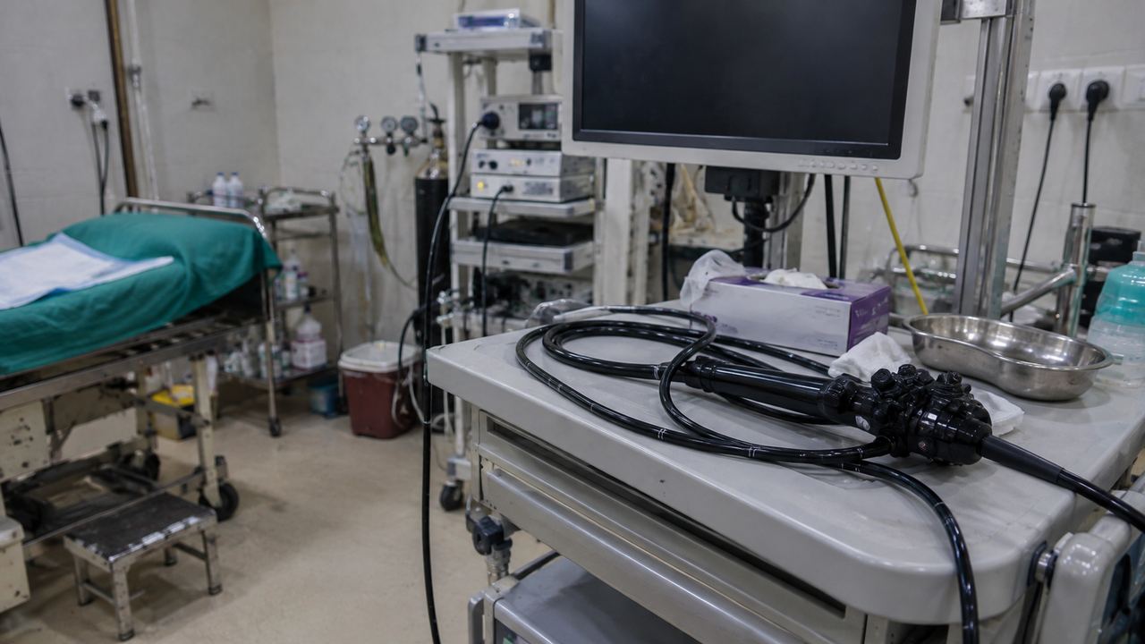 A flexible endoscope coiled on a trolley beside a monitor in a hospital procedure room