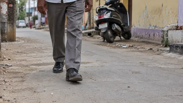A man in trousers and leather shoes walking along a neighbourhood lane